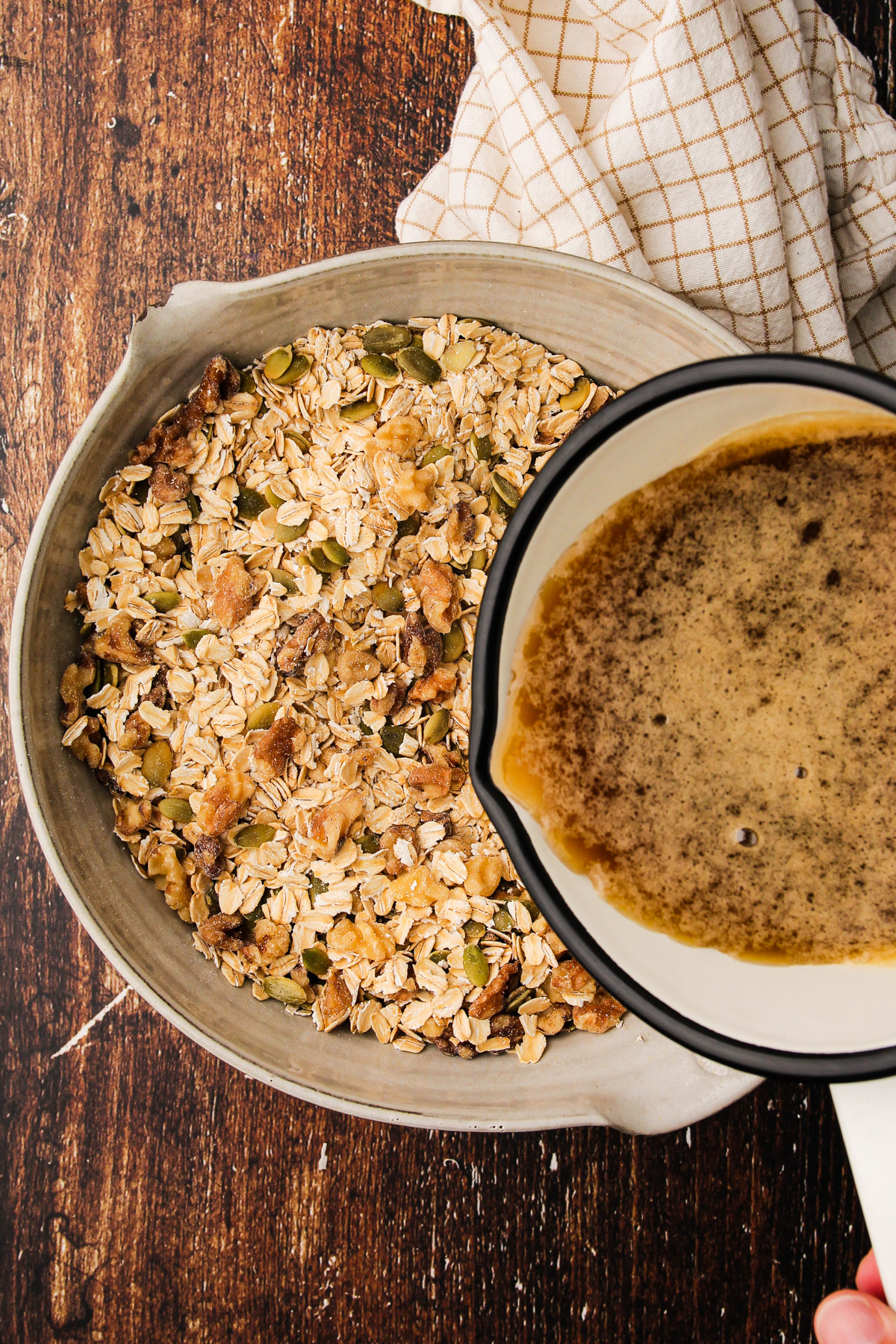 Liquid ingredients for maple walnut granola being poured out of a small saucepan into a bowl of dry ingredients.