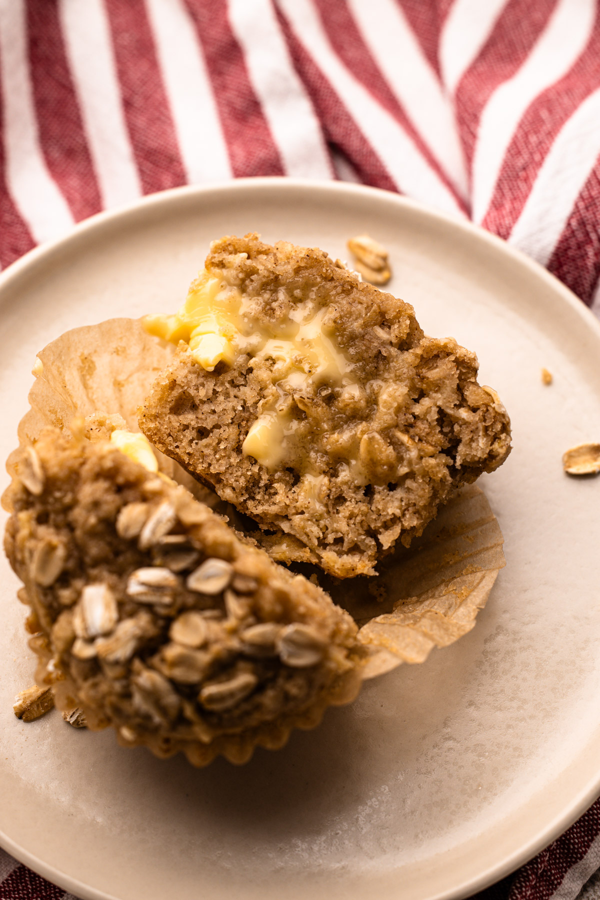 A baked wholesome apple muffin cut in half and spread with melting butter on a plate.
