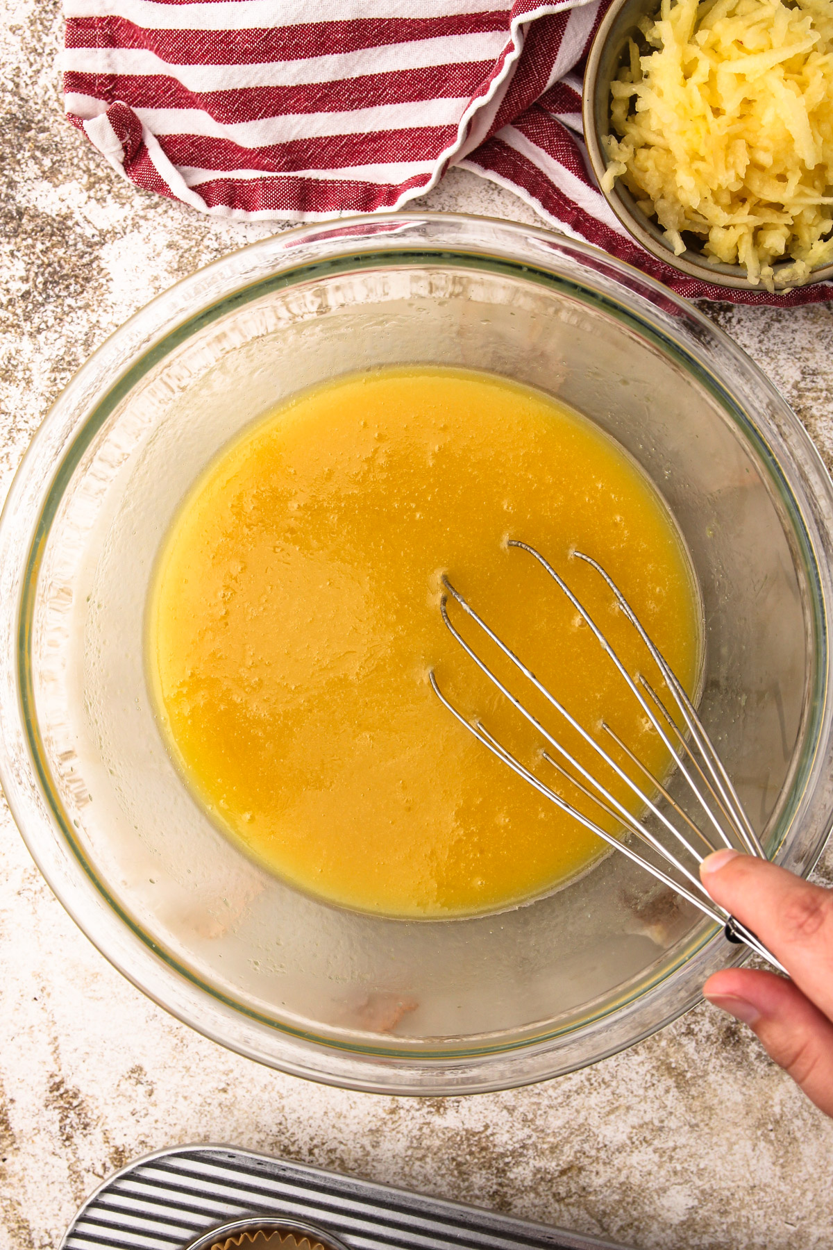 A hand using a whisk to mix together liquid ingredients for wholesome apple muffins in a bowl.