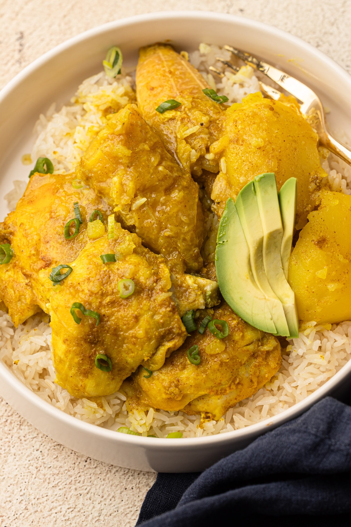A plate of colombian chicken stew with a garnish of green onions and avocado.