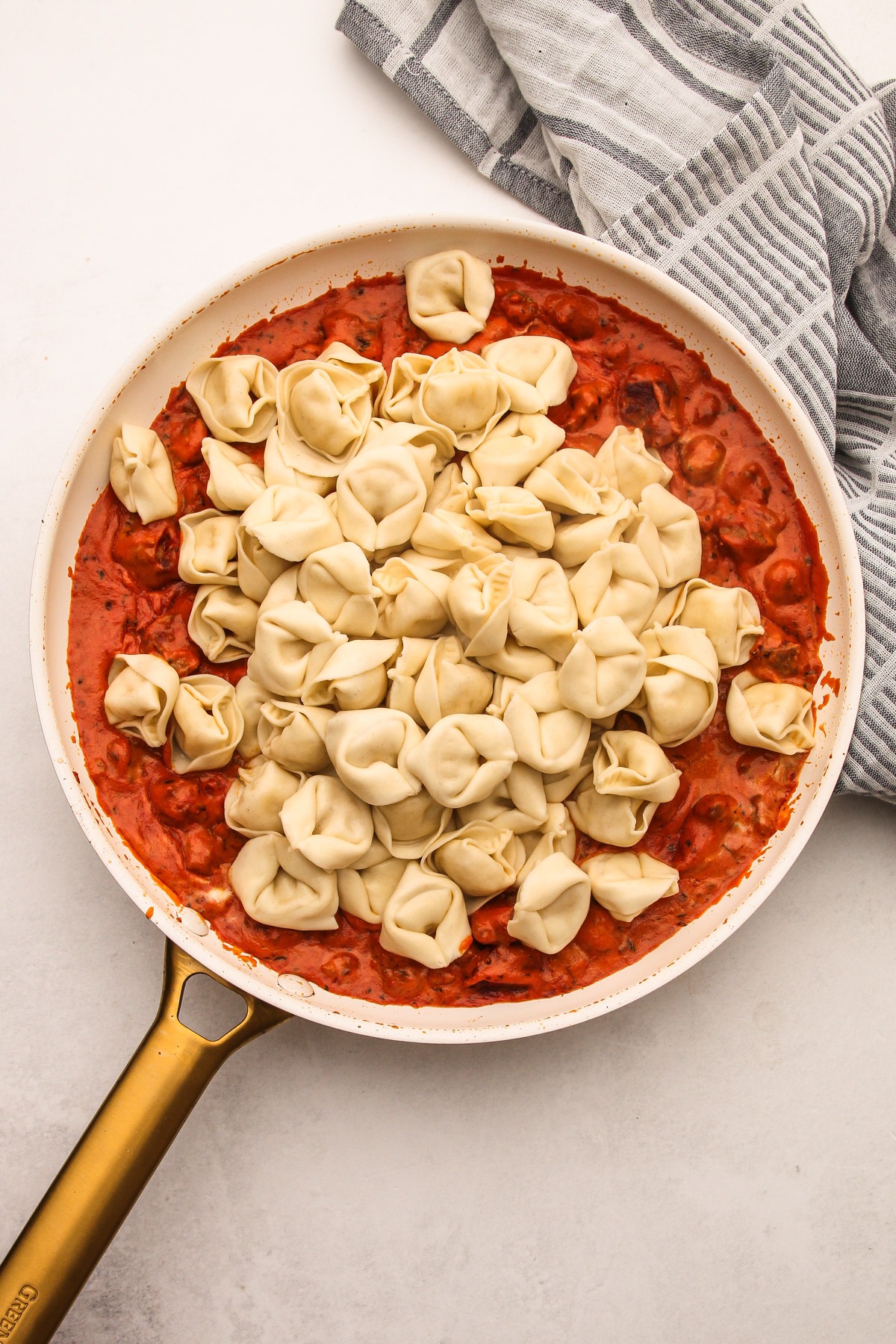 Cooked tortellini being added to a skillet of sauce for creamy tomato tortellini with sausage.