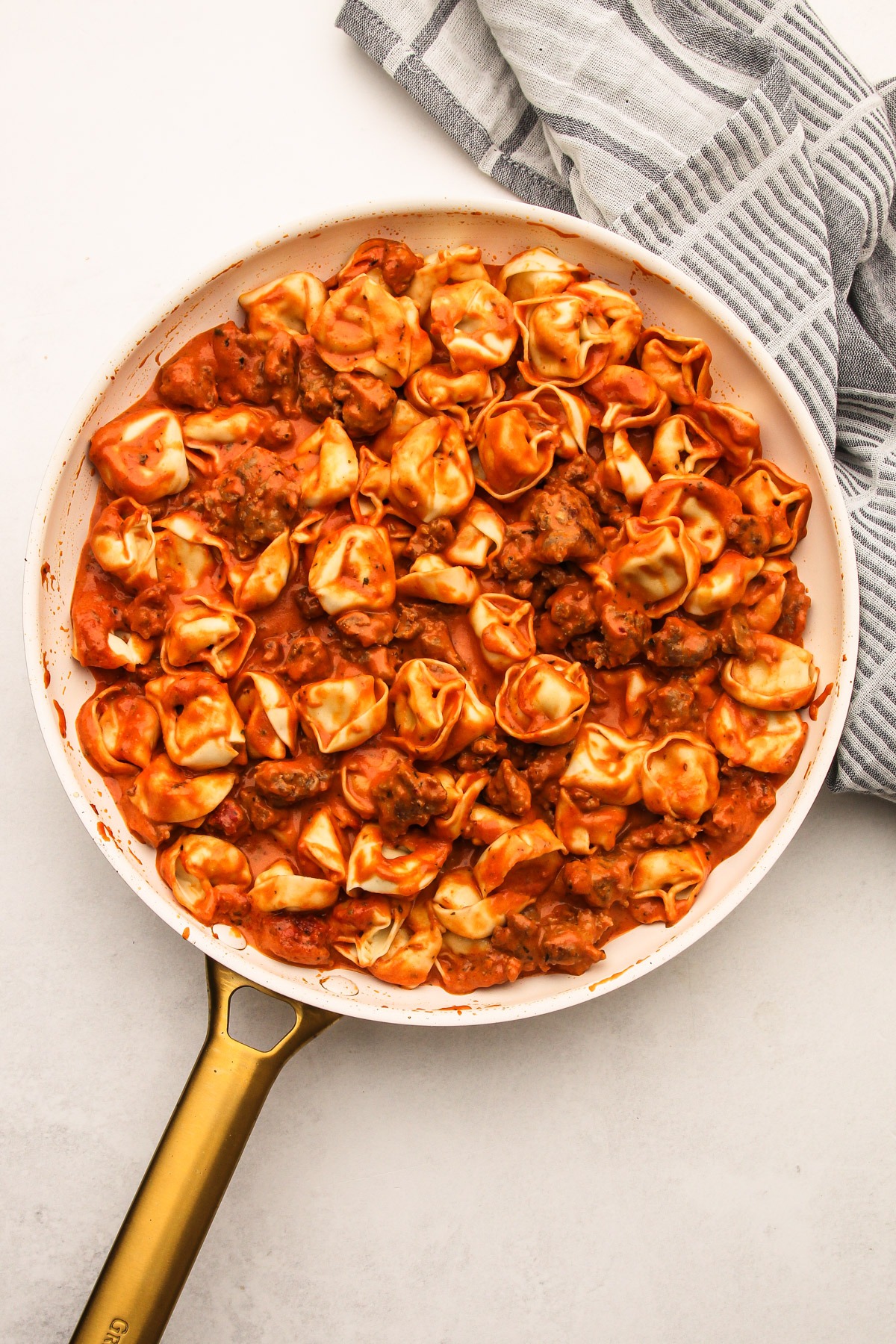 Cooked tortellini stirred into sauce in a skillet for creamy tomato tortellini with sausage.