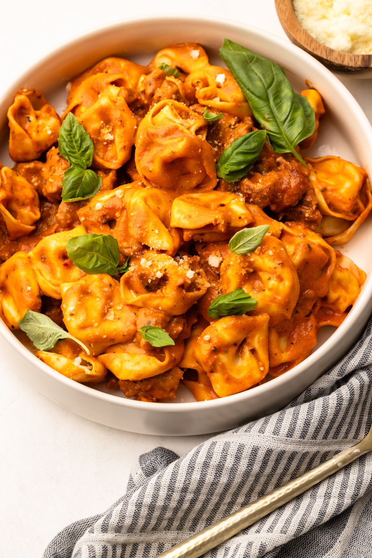 A serving dish of creamy tomato tortellini with sausage, with sprinkles of basil.