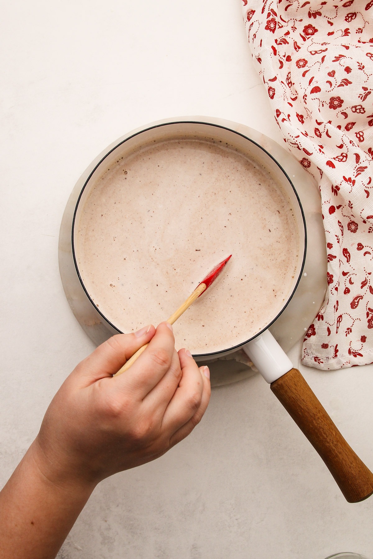 A hand using a rubber spatula to stir together hot chocolate.