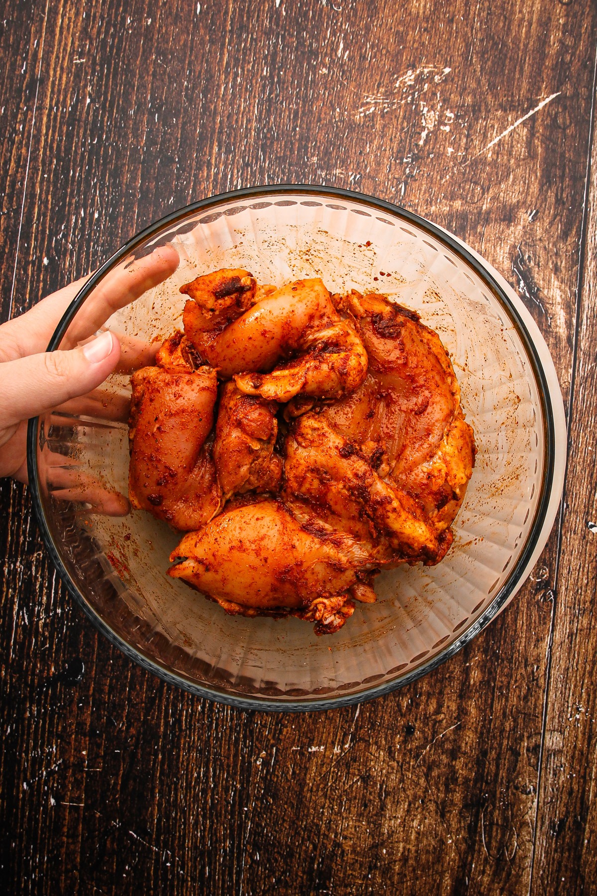 Chicken tossed with seasonings in a bowl for air fryer chicken thighs.