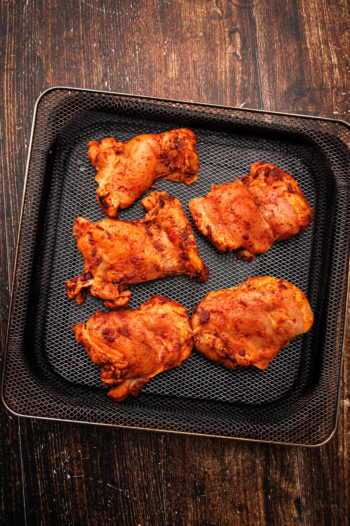 Seasoned chicken in an air fryer basket for air fryer chicken thighs.