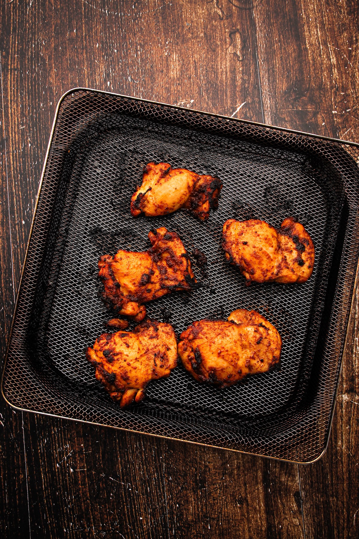 Cooked chicken in an air fryer basket for air fryer chicken thighs.