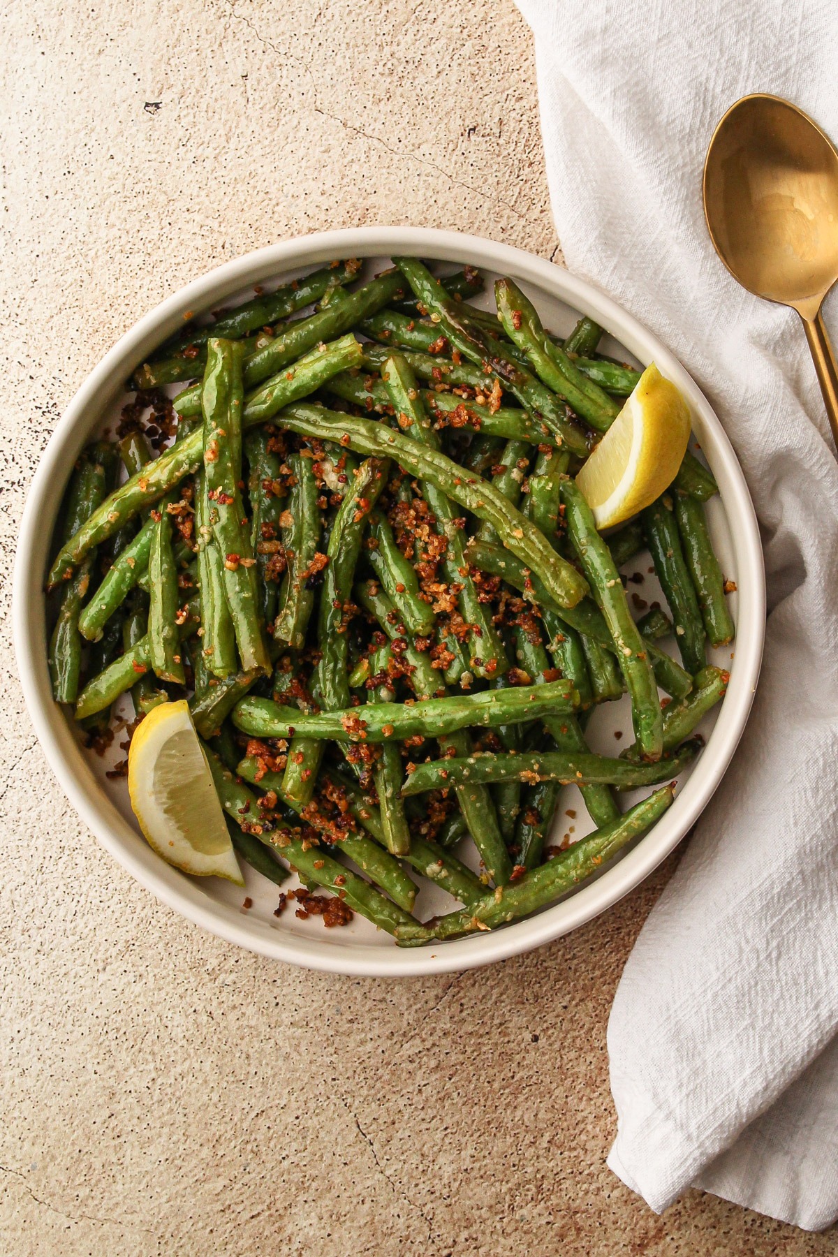 Air fryer green beans with parmesan prepared and served in a bowl with a lemon wedge.