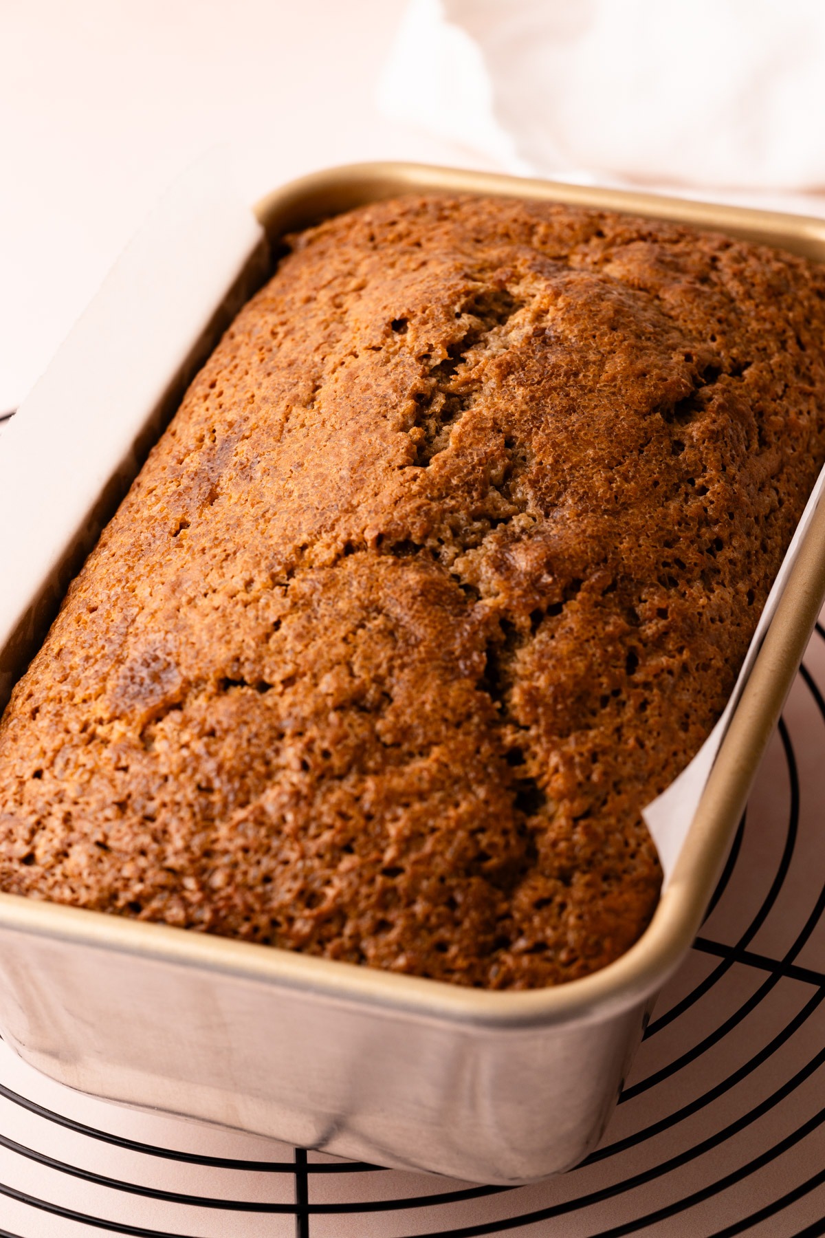 A baked banana bread recipe in a loaf pan on a cooling rack.