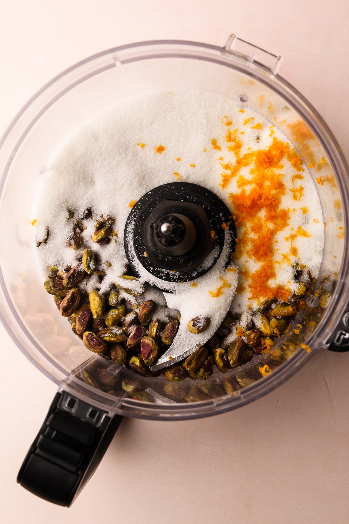 Raw pistachios with sugar and orange zest in a food processor.