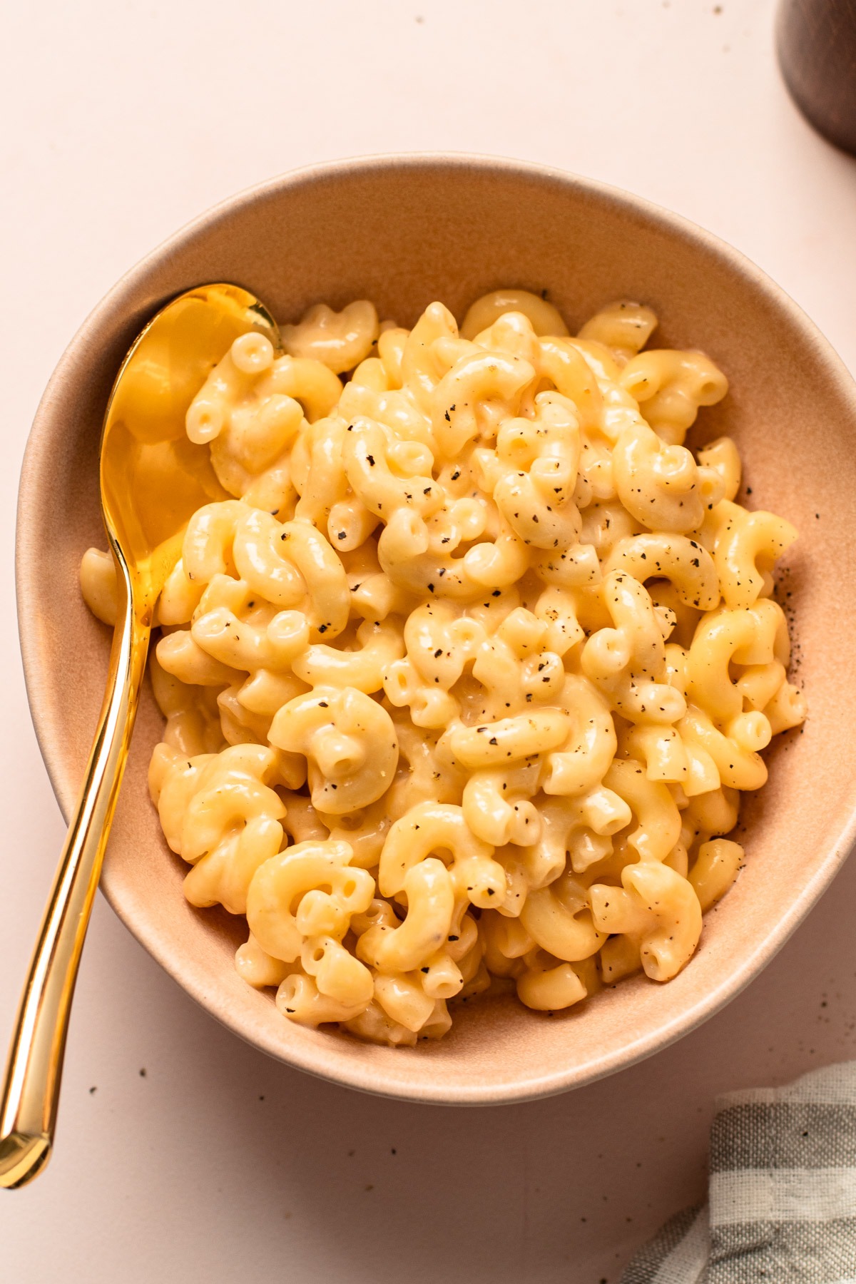 A pink bowl with finished mac and cheese and a sprinkle of pepper.