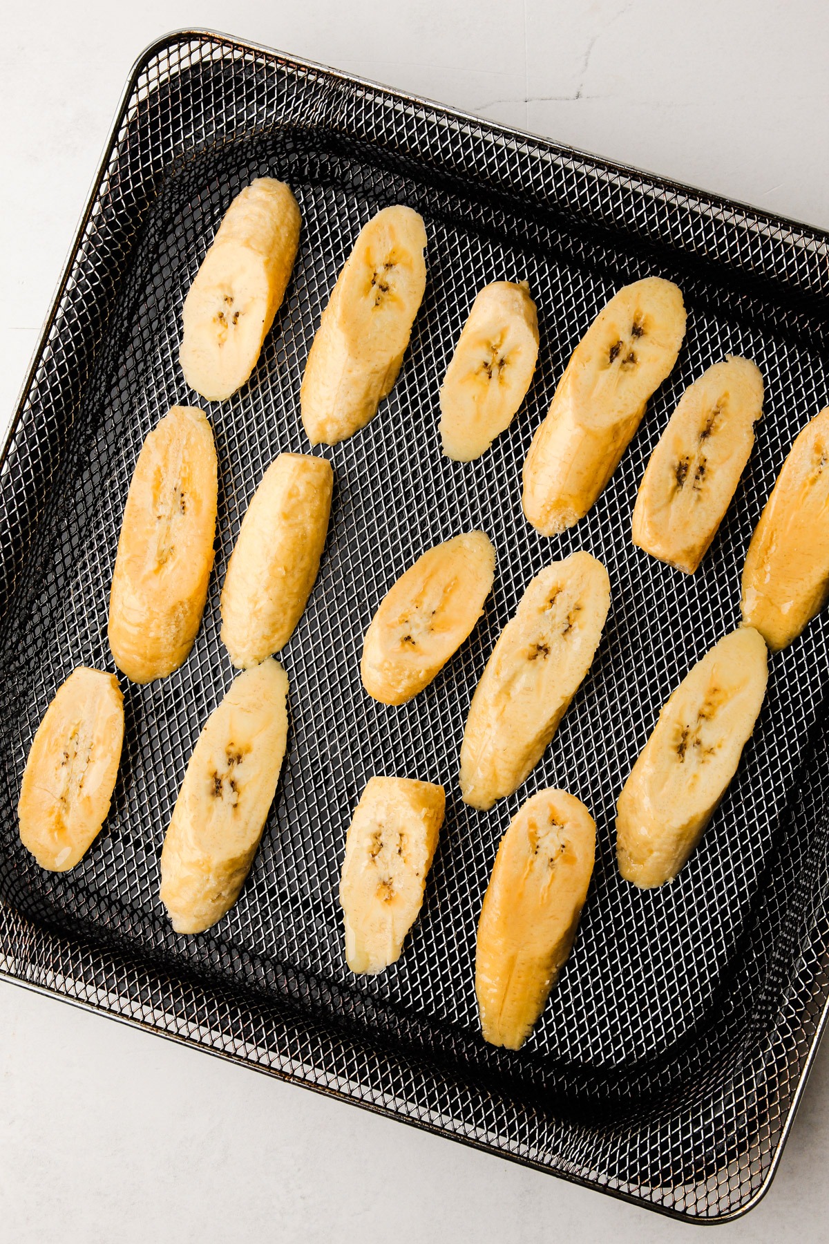 Cut plantains uncooked in an air fryer basket.