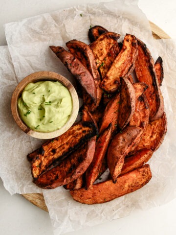 Plated cooked air fried sweet potato wedges on a serving platter with a side of avocado dip.