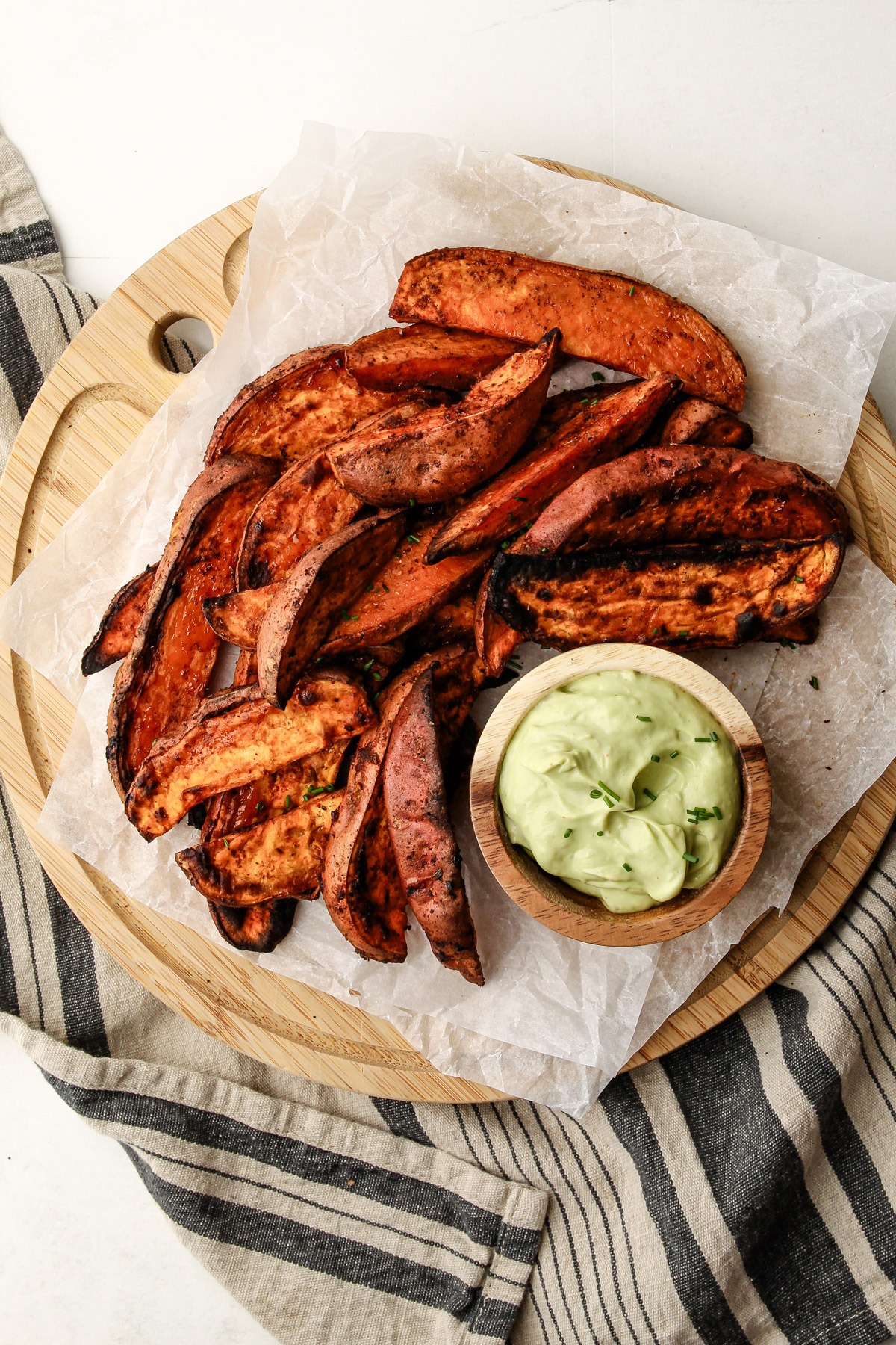 Plated cooked air fried sweet potato wedges on a serving platter with a side of avocado dip.