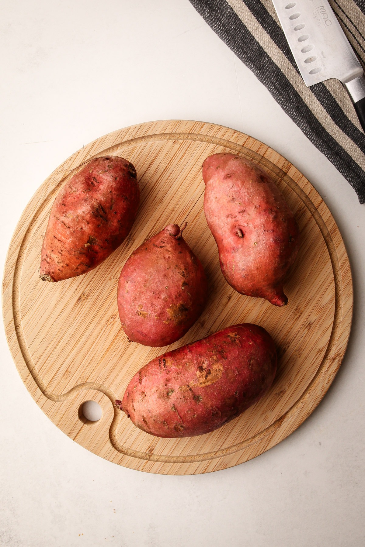 Cleaned and scrubbed sweet potatoes on a cutting board.