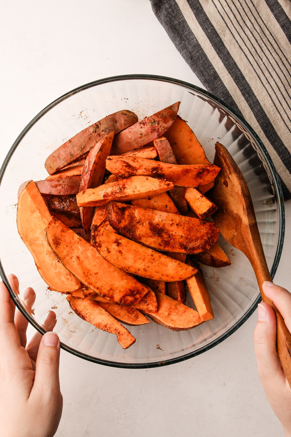 Tossing together cut sweet potato wedges in a bowl with spices, salt and oil.