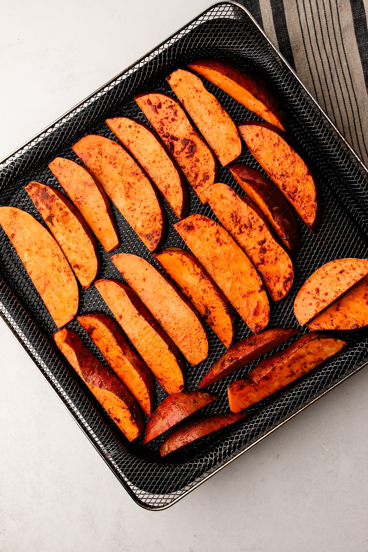 Seasoned and uncooked sweet potato wedges on an air fryer basket.