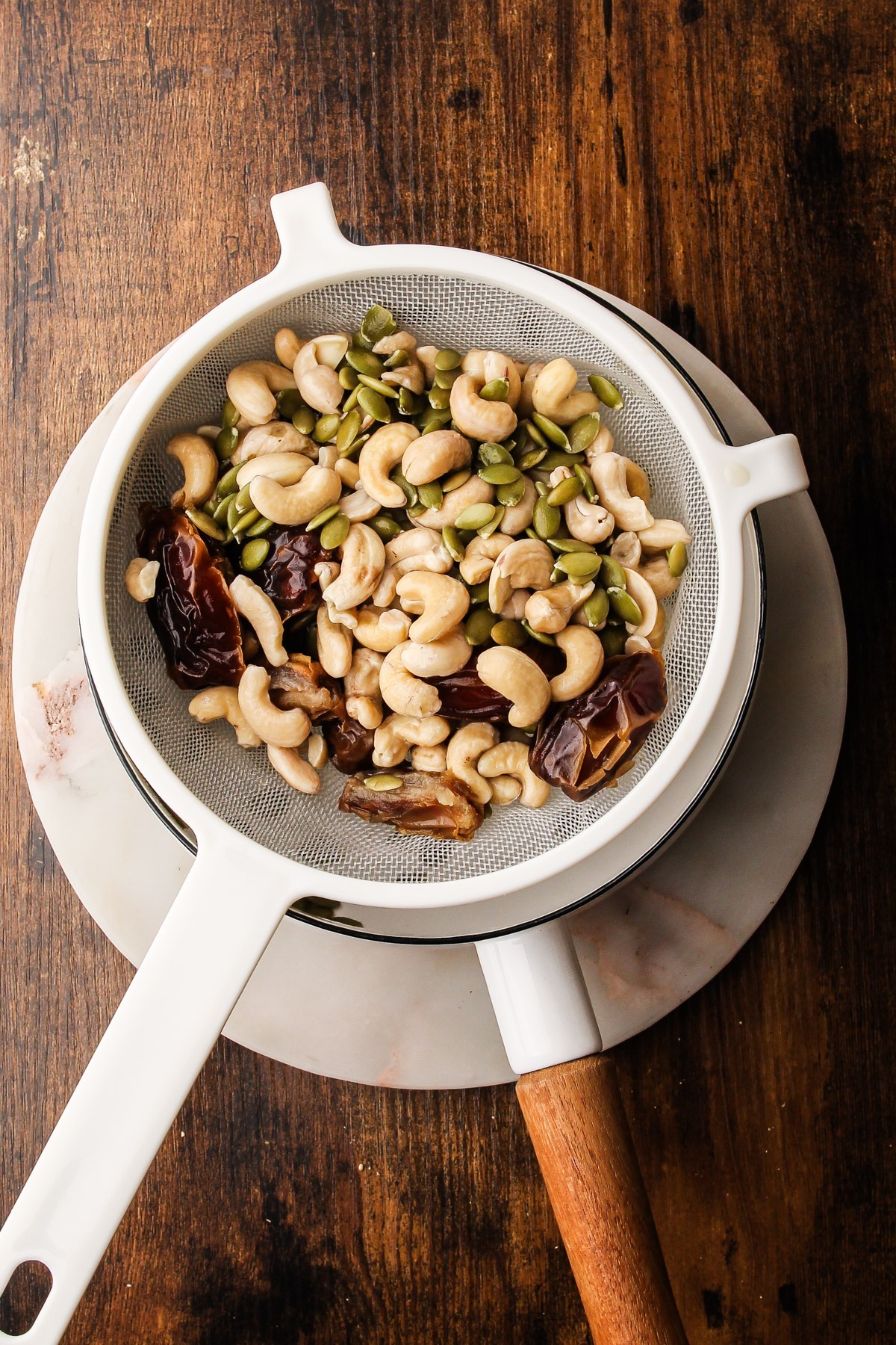 Soaked dates, cashews and pumpkin seeds draining in fine mesh strainer.