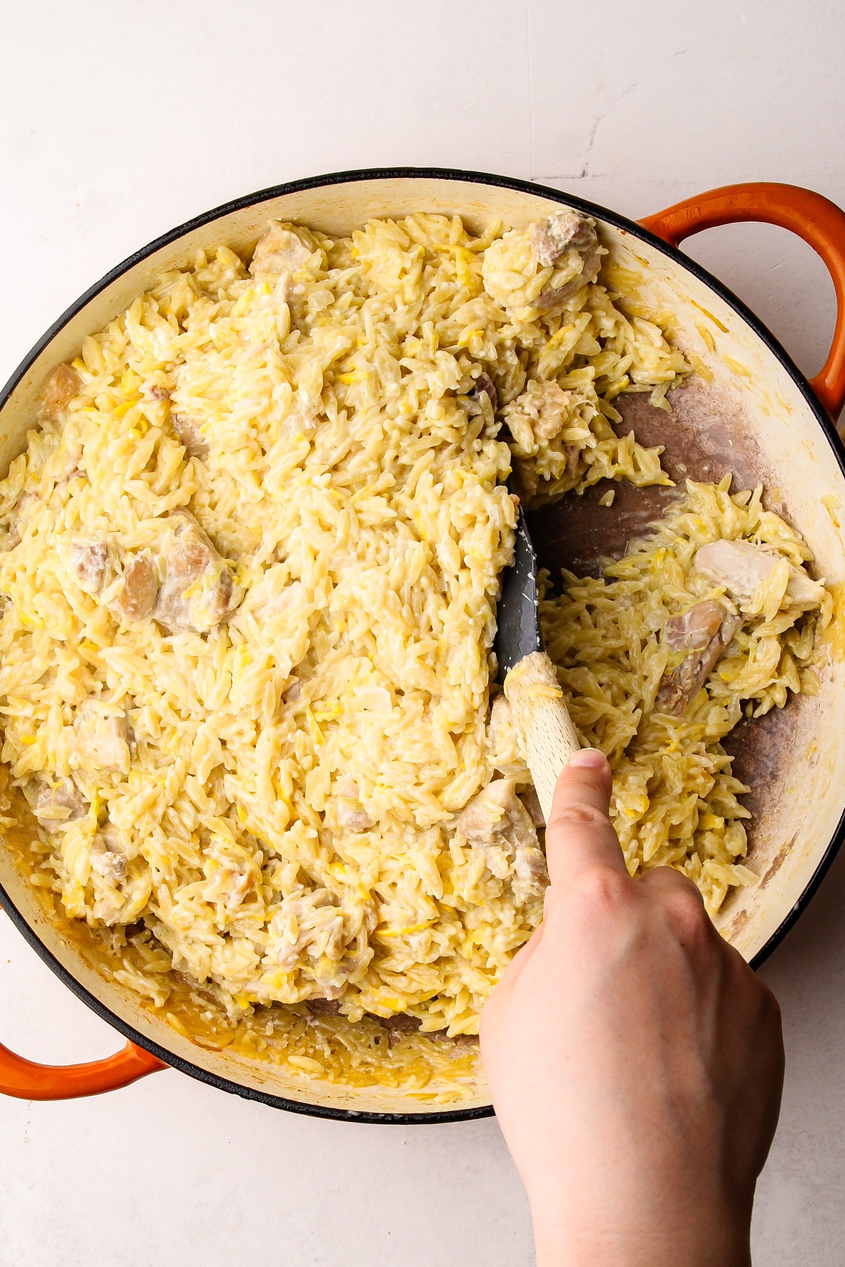 Mixing lemon chicken orzo pasta in a skillet with feta and squash.