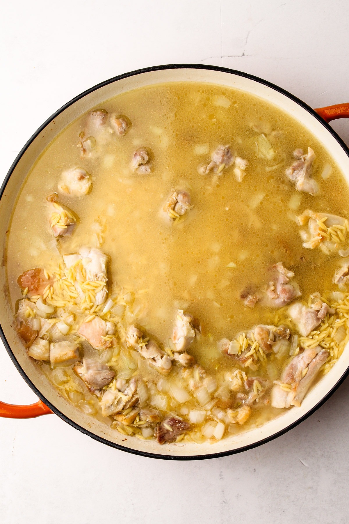 Preparing lemon chicken orzo pasta with feta in a skillet.