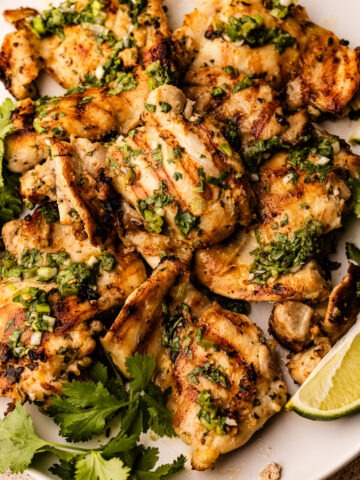 A platter of cilantro lime chicken thighs with extra cilantro and lime.