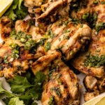 A platter of cilantro lime chicken thighs with extra cilantro and lime.