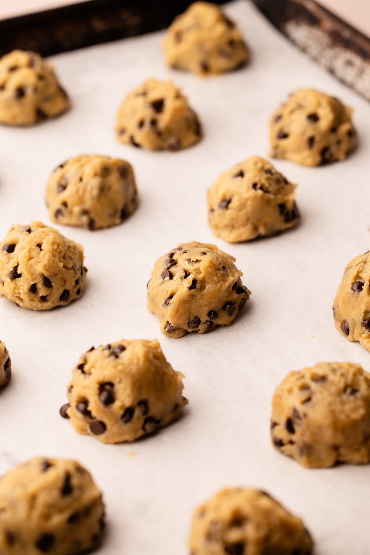 Chocolate chip cookie dough balls on a sheet pan.