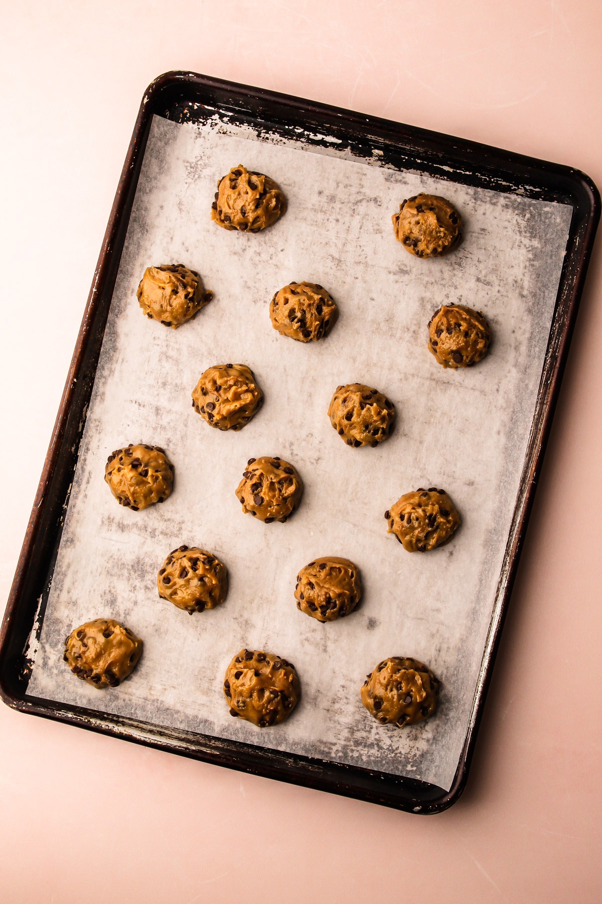 Scooped chocolate chip cookie dough unbaked on a sheet pan.