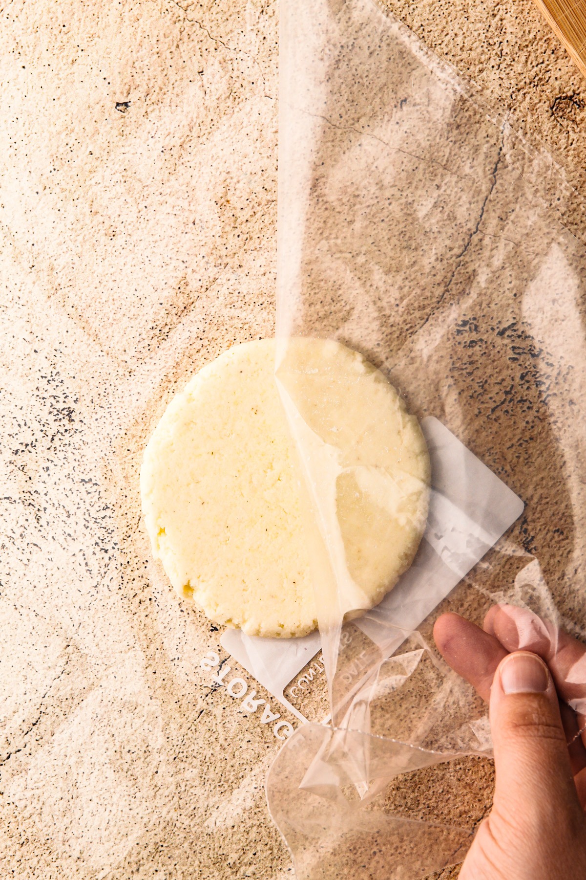 Removing the plastic from a flattened arepa dough disk.