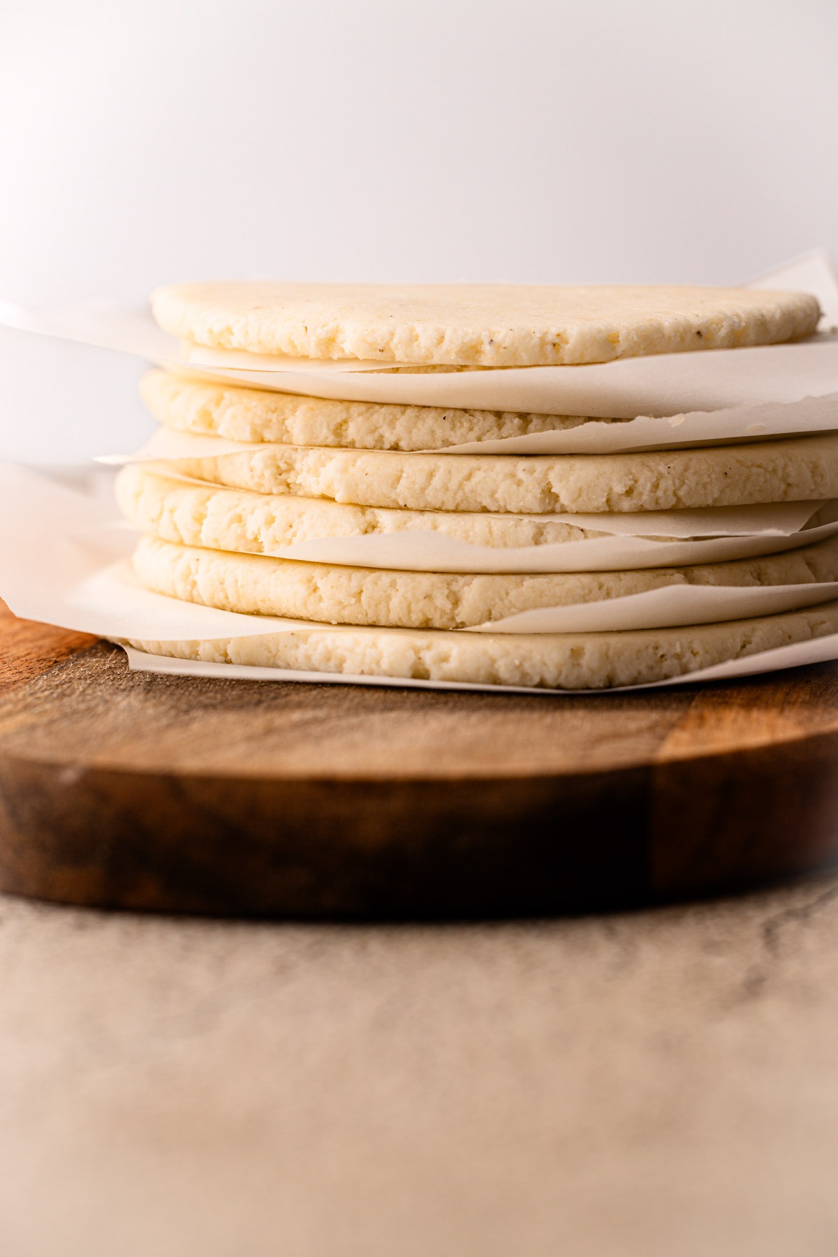 Thin stacked uncooked arepas between pieces of parchment.