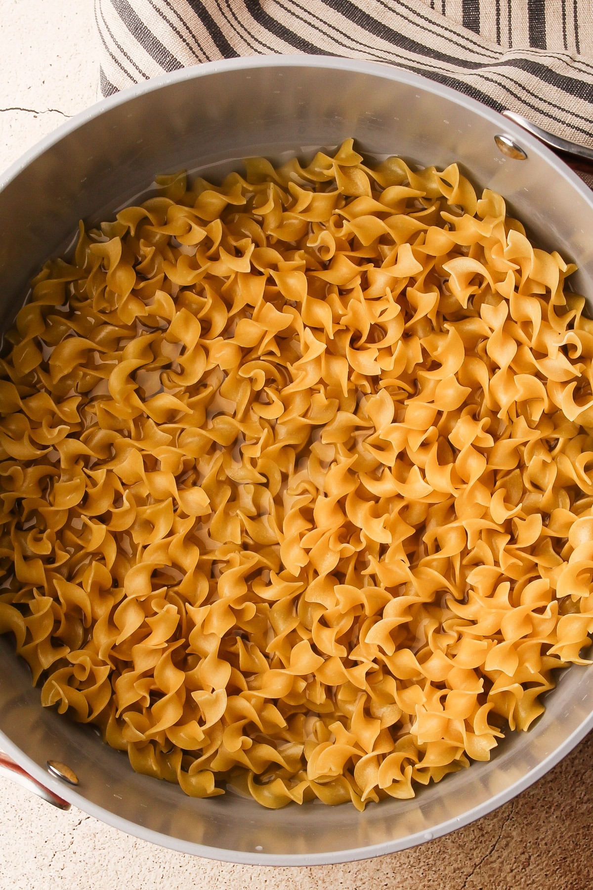 Uncooked egg noodles in a pot with a little bit of water.