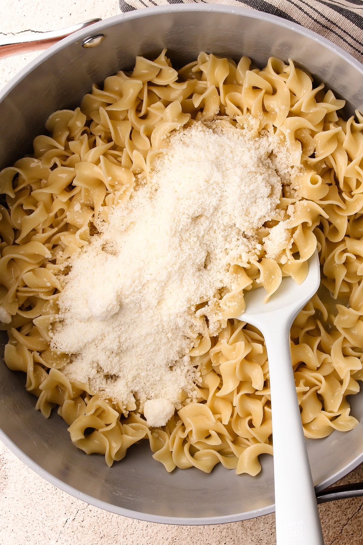 Parmesan cheese sprinkled over egg noodles in a pot.