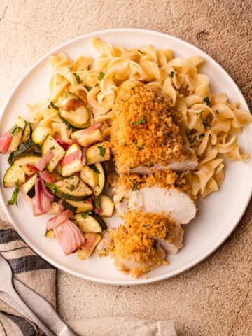 A serving plate of ritz cracker chicken with buttered egg noodles and salad.