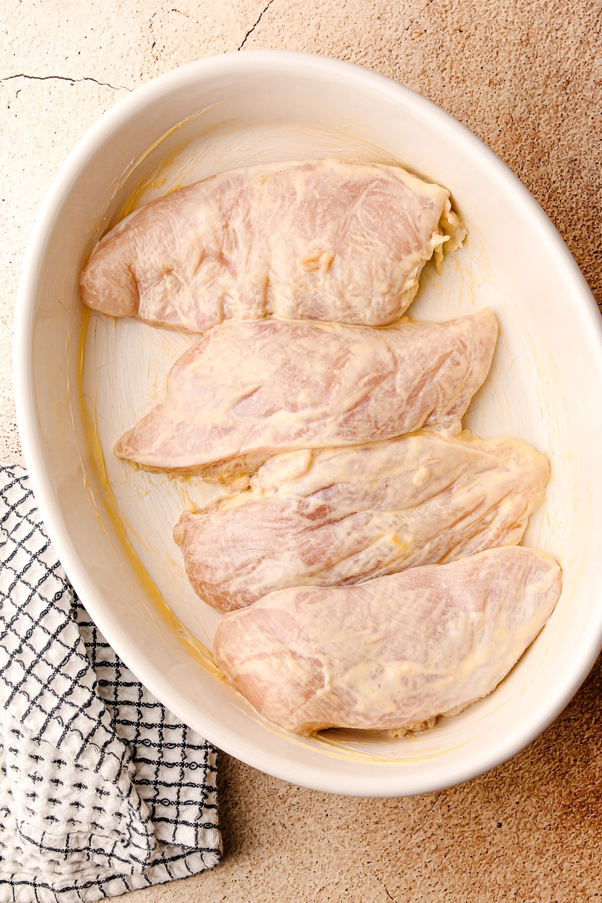 Chicken breasts in marinade in a baking dish.