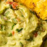 A bowl of colombian guacamole with a plantain chip dipping into it.