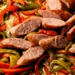 Sliced sausages baked in the oven with peppers and onions on a sheetpan.