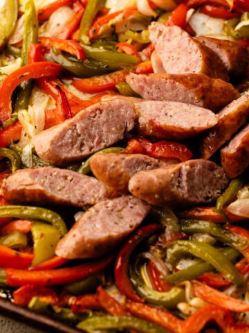 Sliced sausages baked in the oven with peppers and onions on a sheetpan.