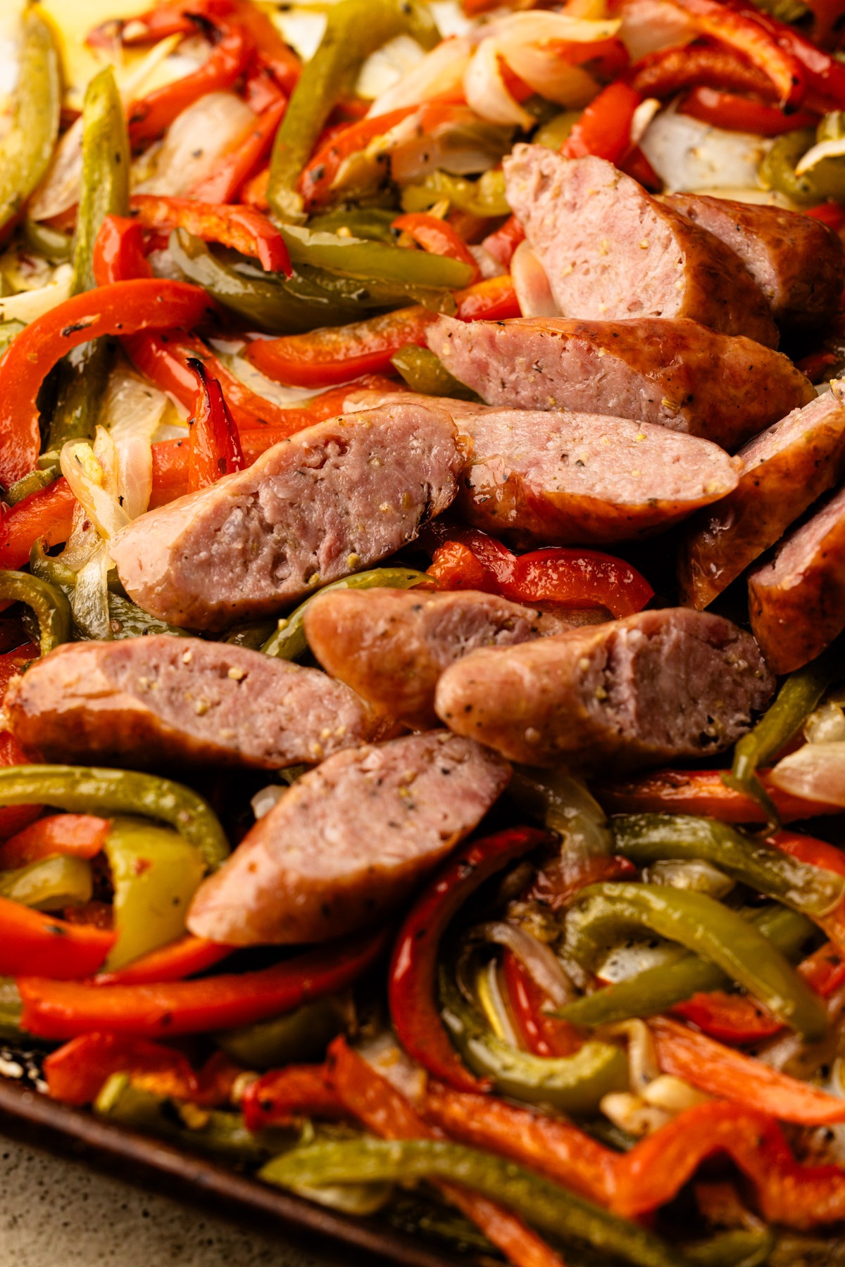 Sliced sausages baked in the oven with peppers and onions on a sheetpan.