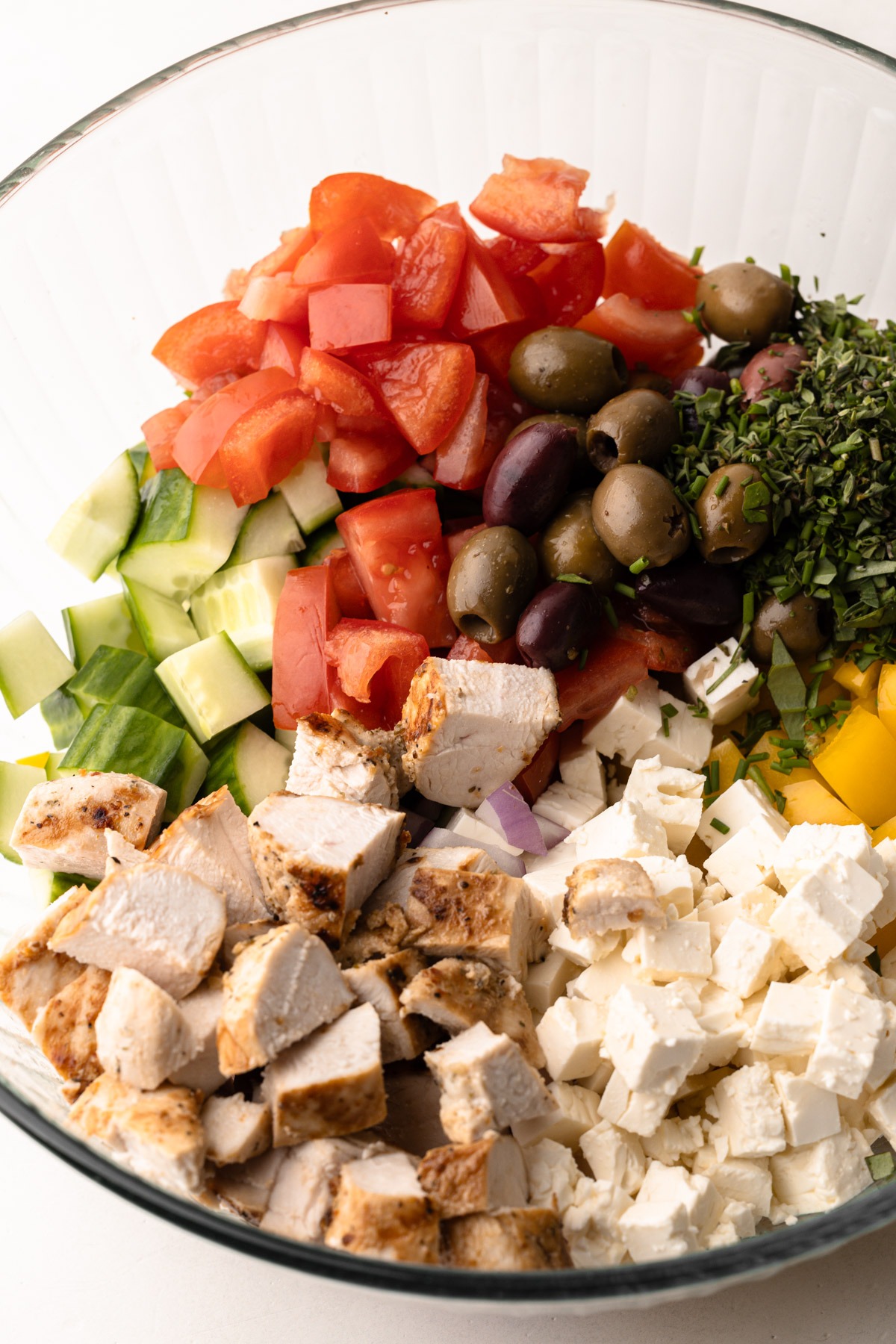 A bowl with greek chicken salad ingredients chopped up.