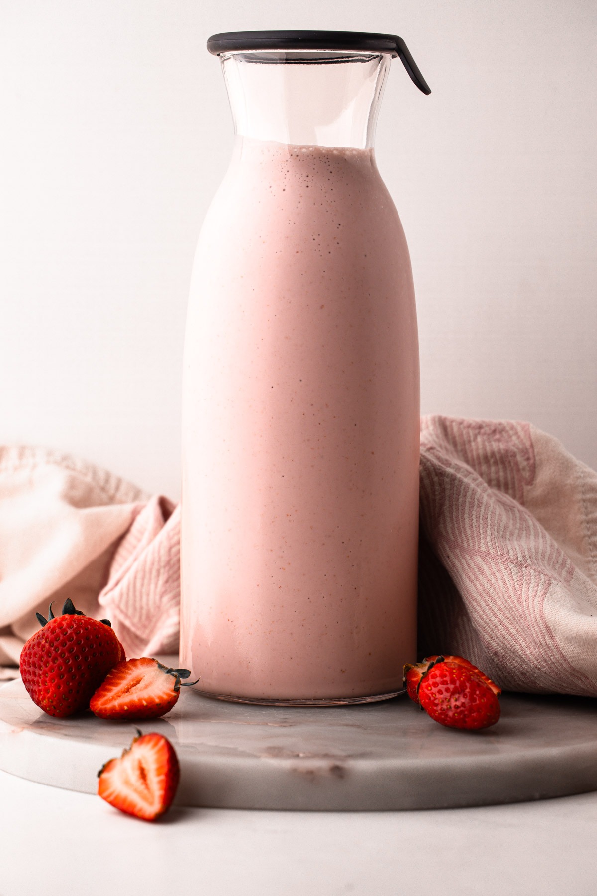 A bottle of homemade strawberry milk with fresh strawberries.