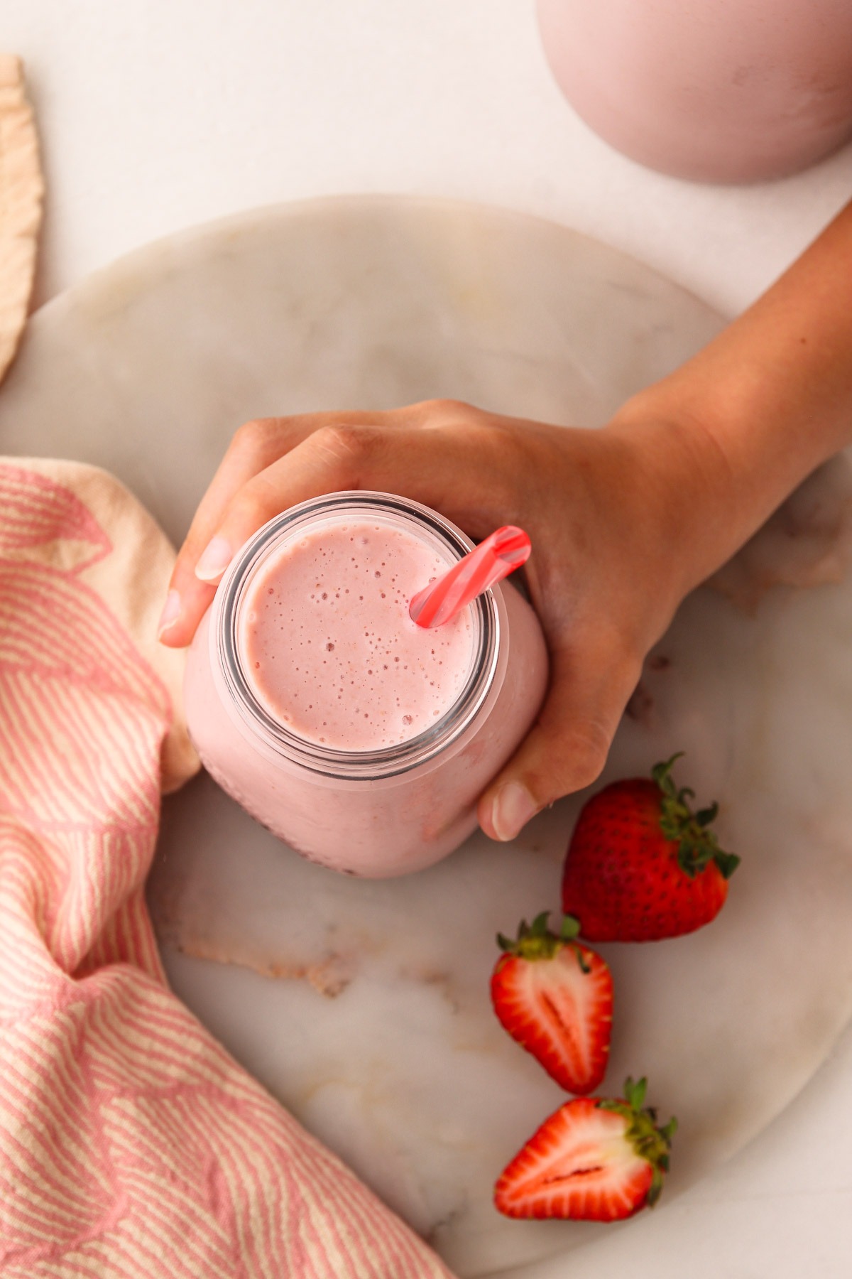 A hand holding a cup of homemade strawberry milk with a straw in it.