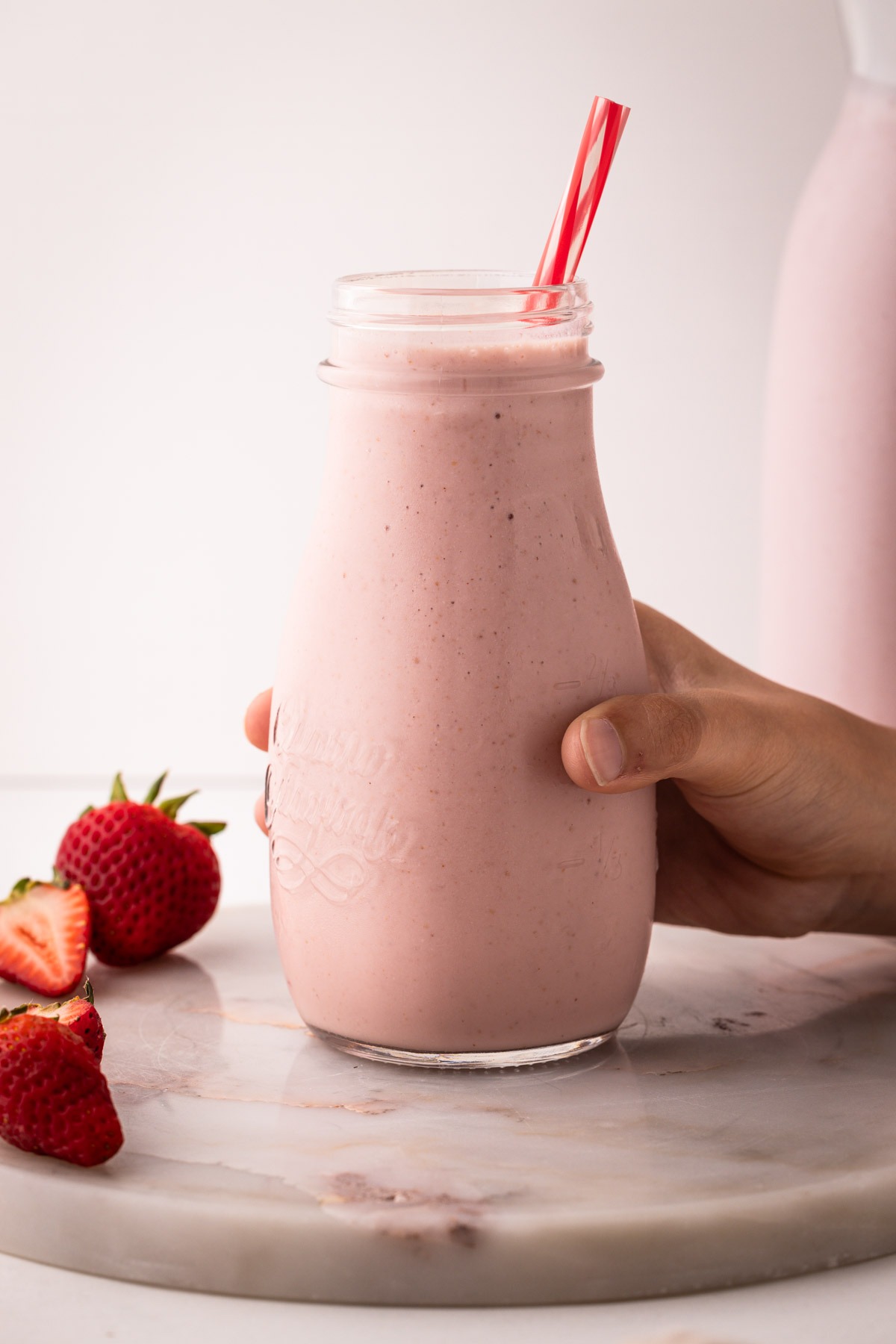 A hand holding a filled glass of strawberry milk made from scratch.