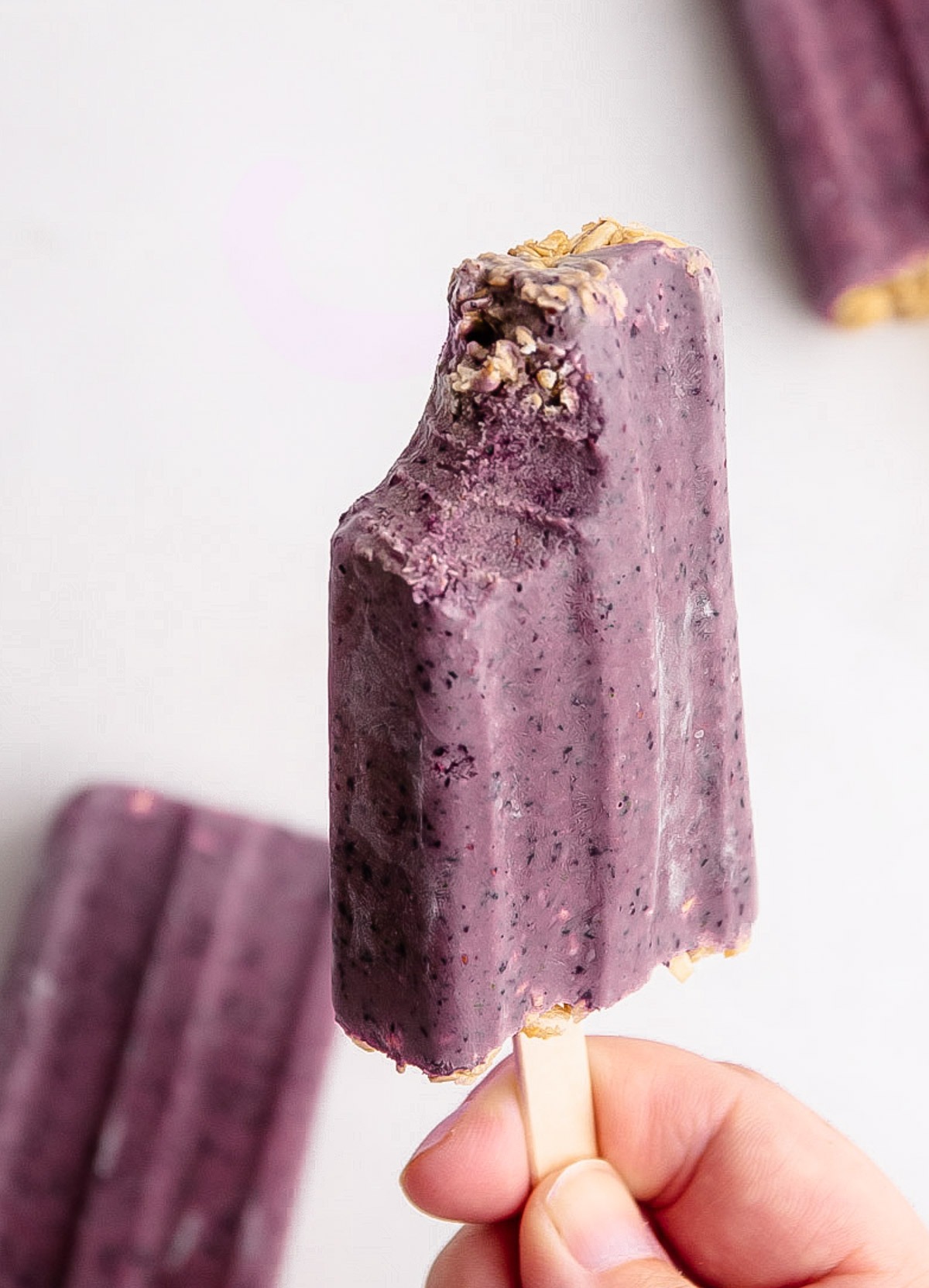 A breakfast popsicle made from fruit, yogurt and granola with a bite taken from it.