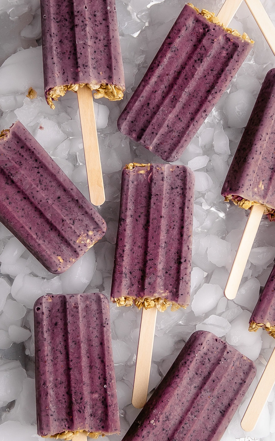 Breakfast popsicles made from blueberries, yogurt and granola on a tray of ice.