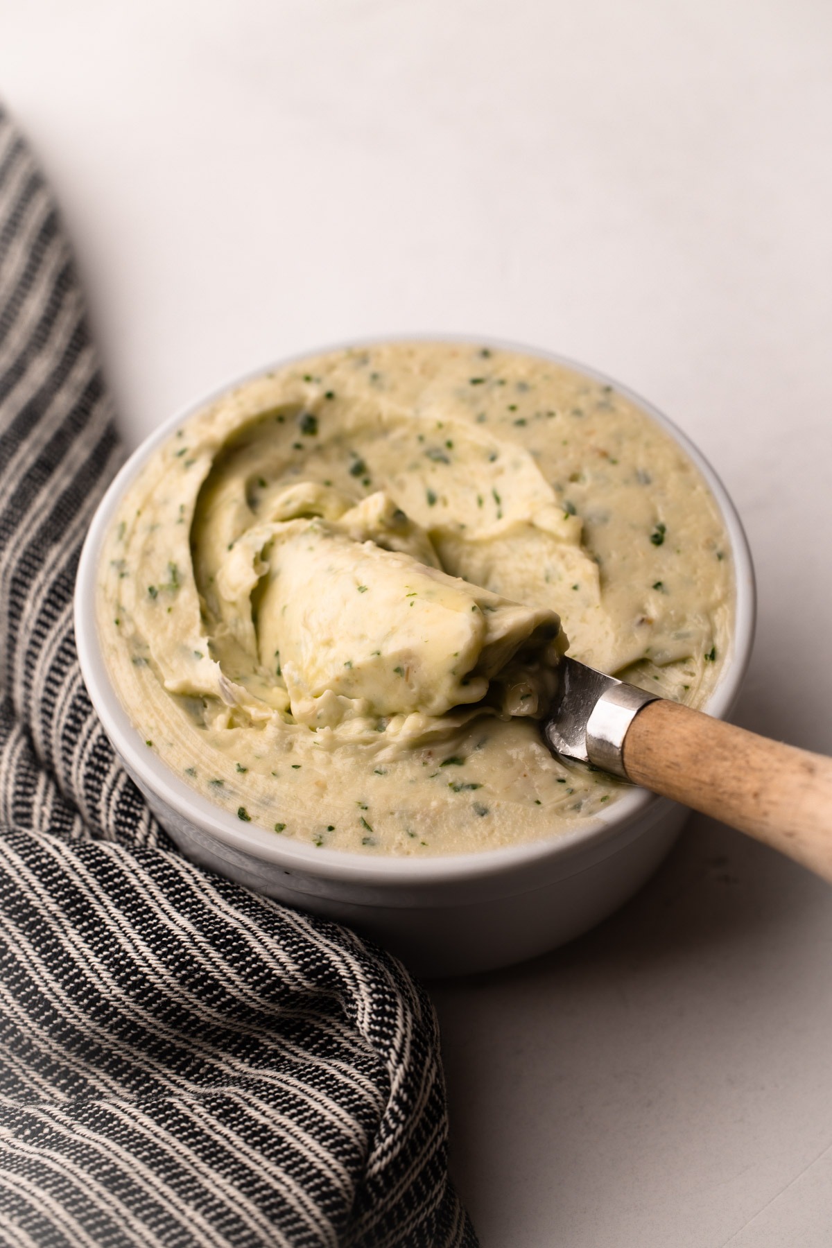 A small dish of garlic herb butter with a striped cloth underneath.