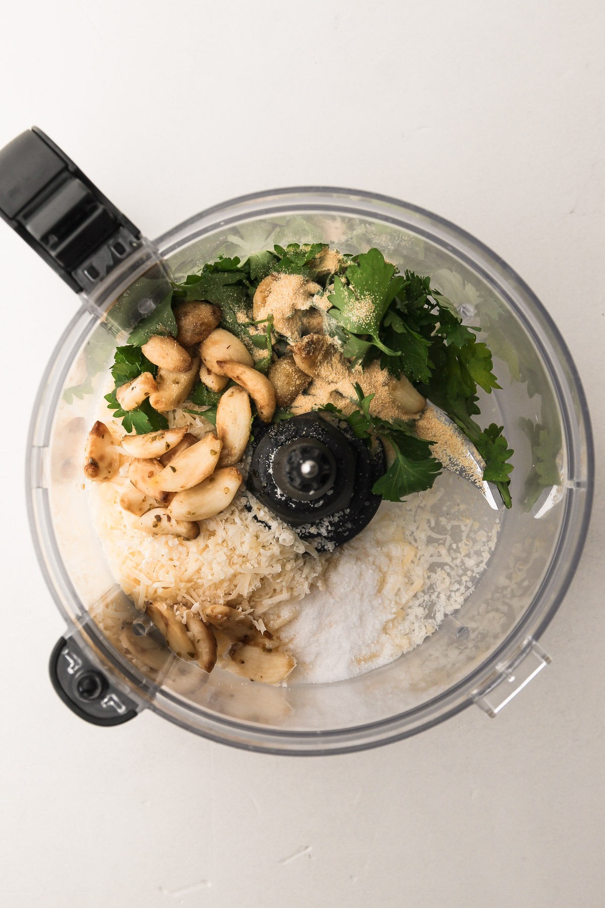 Ingredients for garlic butter, including garlic, parsley, and parmesan in a food processor.