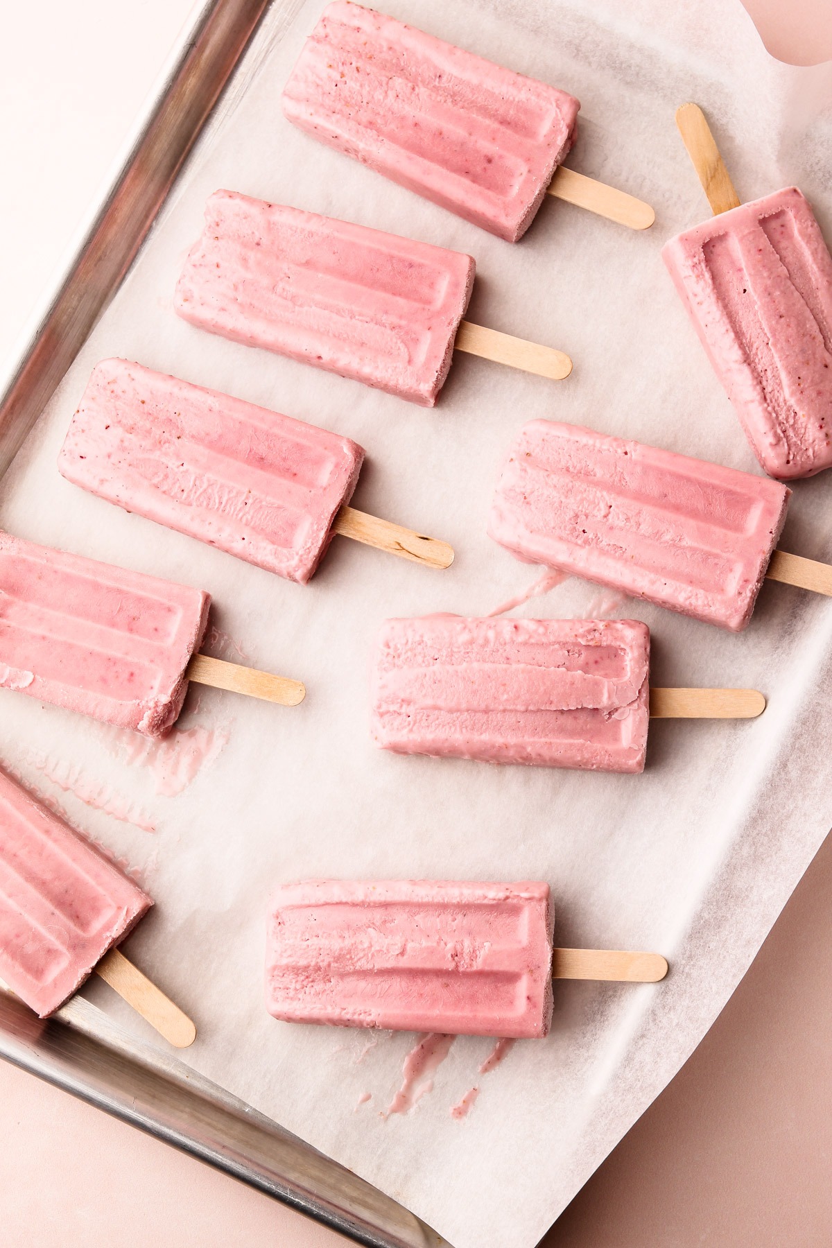 A tray of pink strawberry shortcake popsicles on parchment paper.