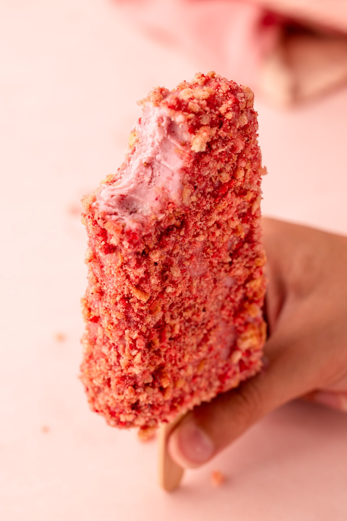 Close-up of a strawberry shortcake popsicle with a bite taken out.