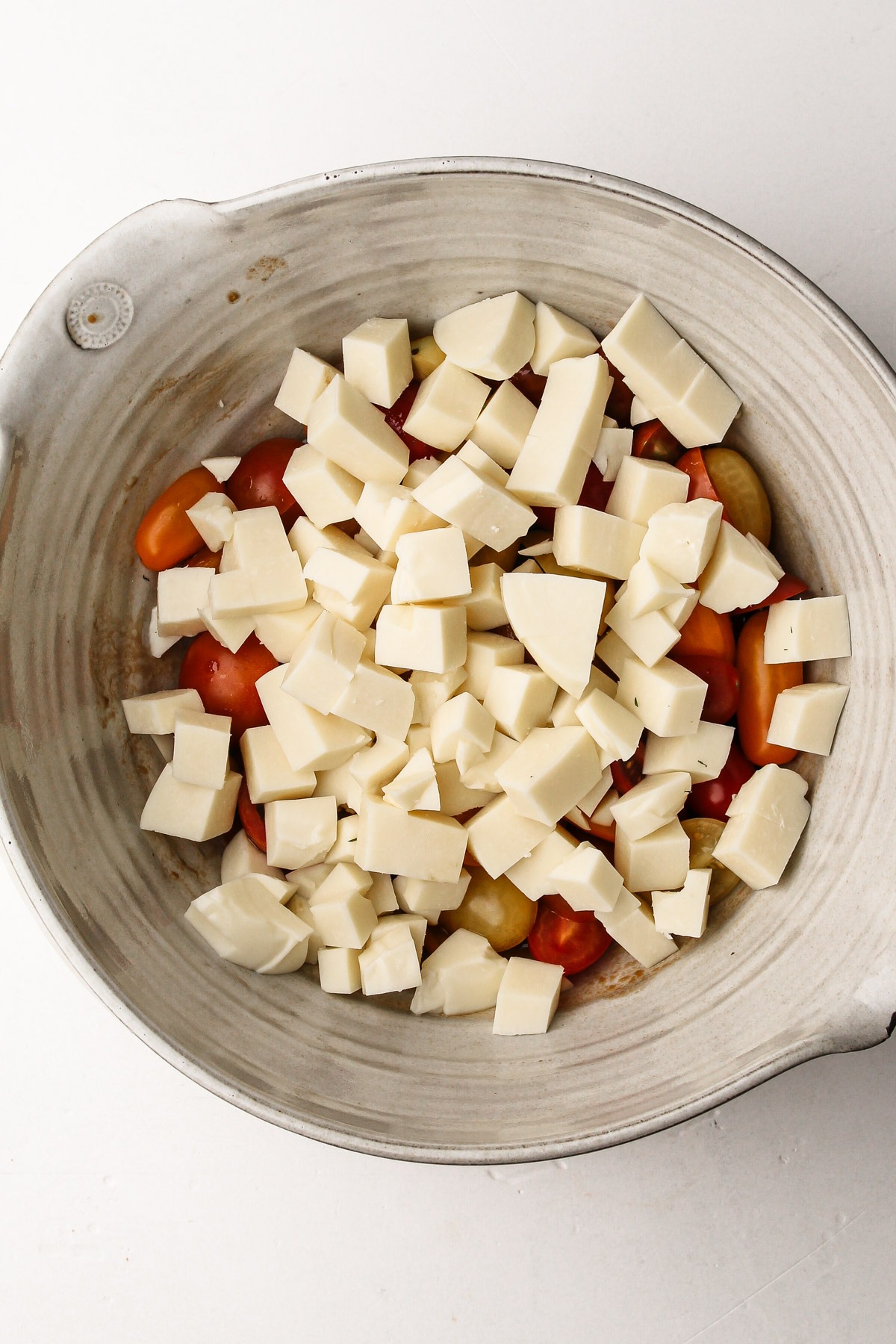 Adding cubed cheese to marinated tomatoes for a panzanella caprese salad.