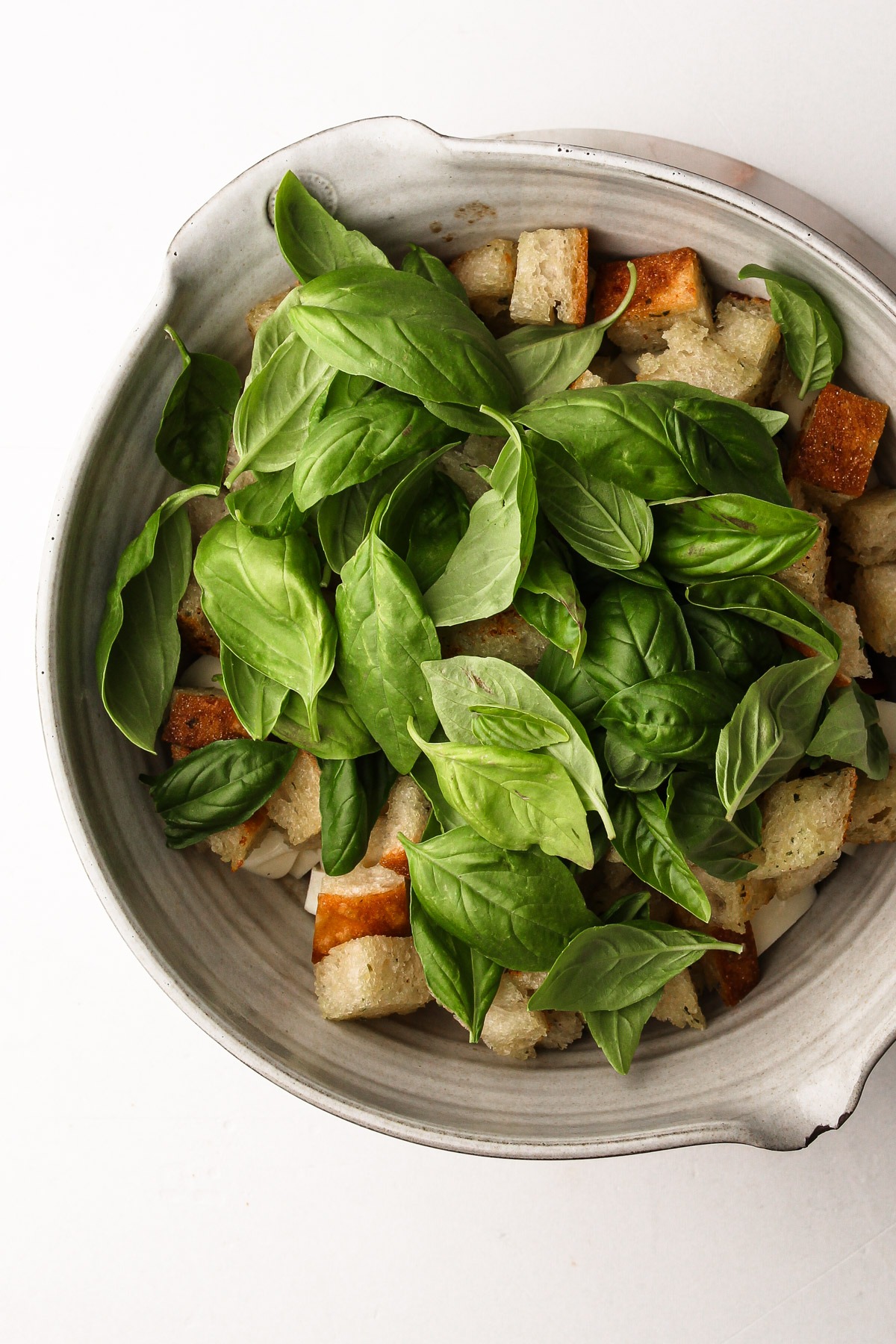 Fresh basil leaves covering the croutons in a caprese panzanella.